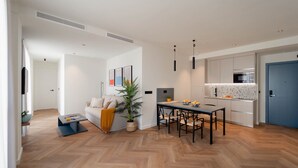 A modern living room with a sofa, coffee table, and a dining area with a table and chairs. There is a kitchen with a microwave and cabinets. - NIU Line (Villajoyosa)