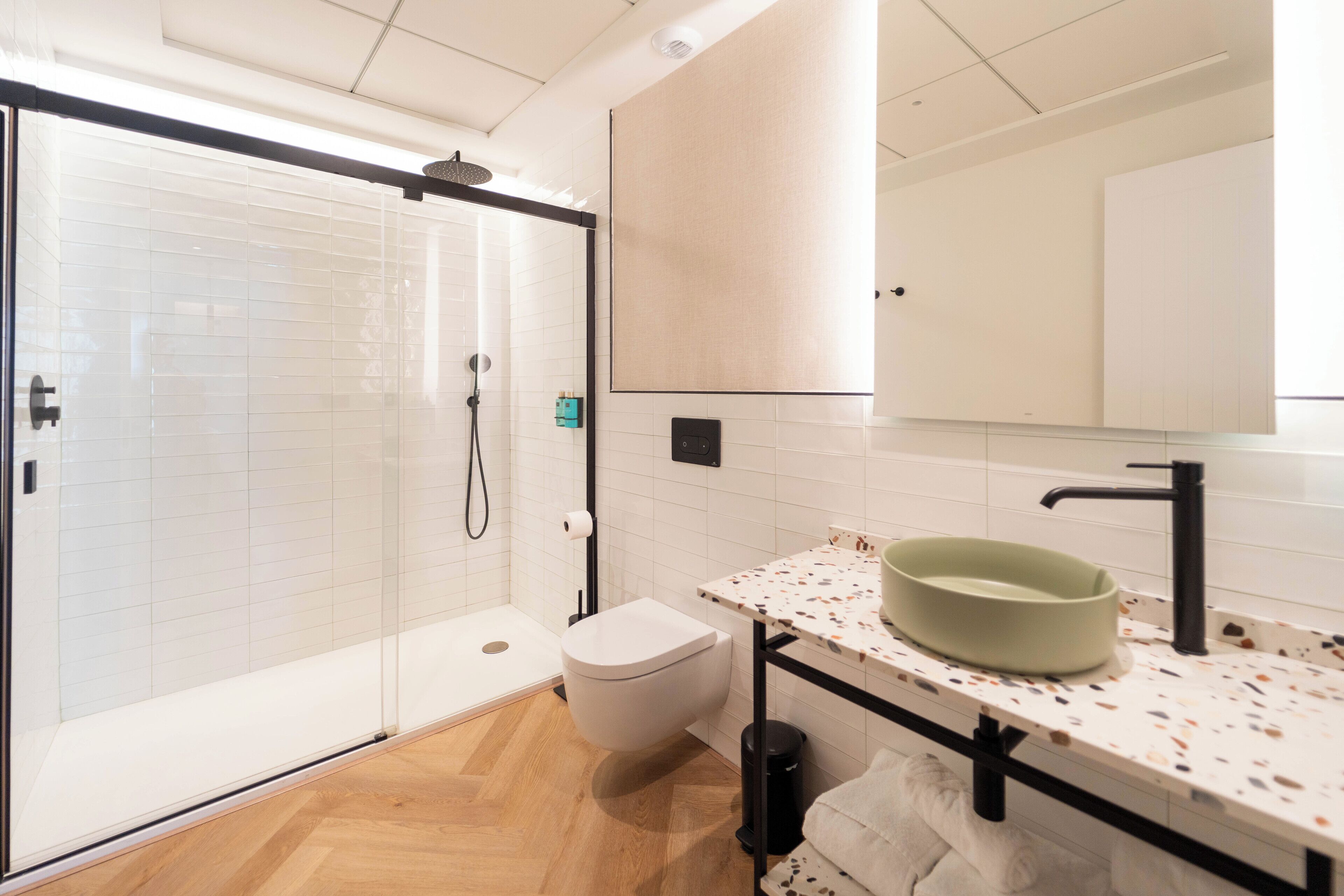 Un bagno moderno con box doccia in vetro, un WC bianco, un lavabo con piano di appoggio maculato e uno specchio sopra il lavabo.