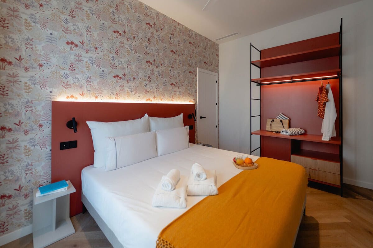 A hotel room with a bed, a bedside table, a wardrobe, and a wall with floral wallpaper.