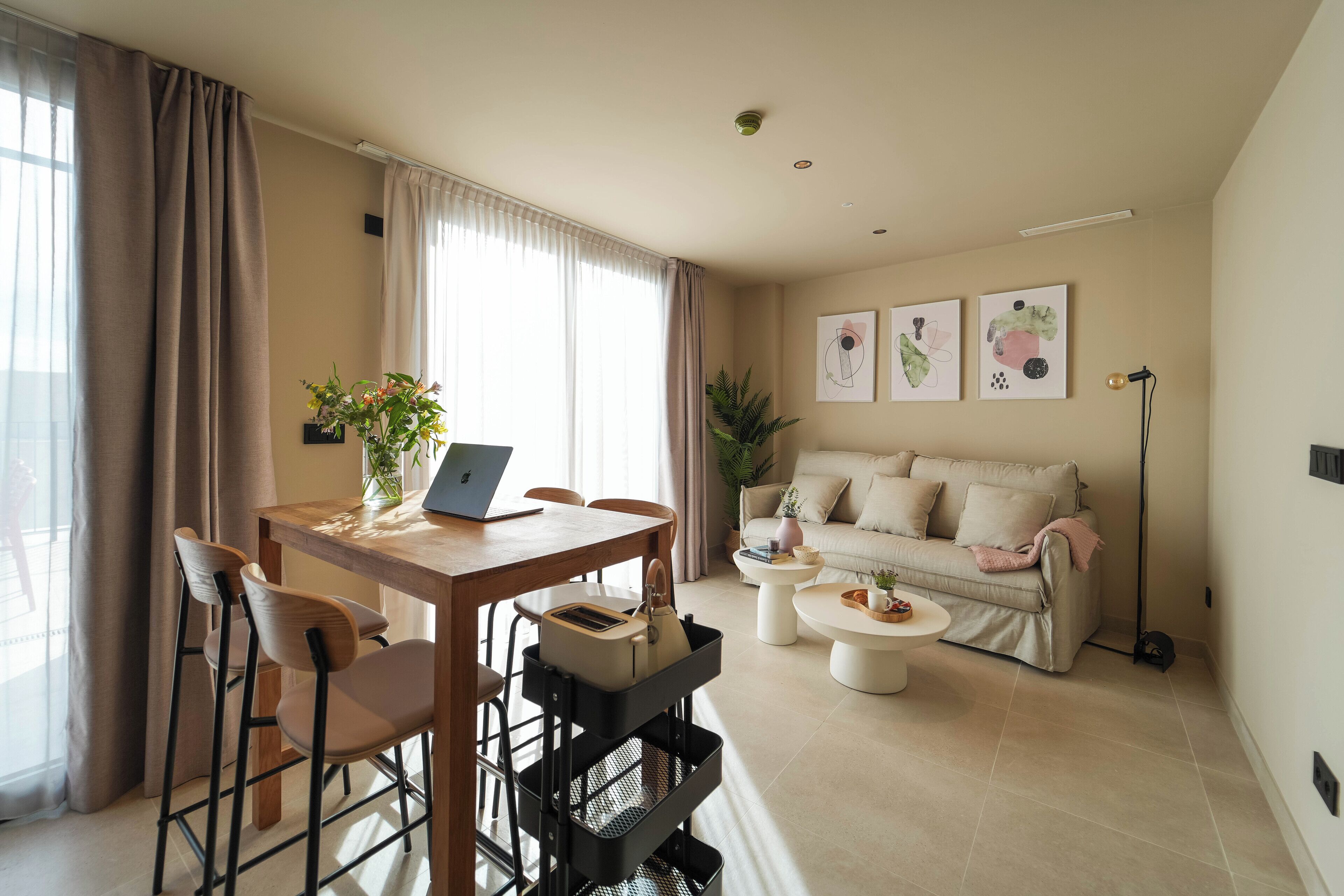 A modern living room with a dining area, a sofa, and a coffee table. There is a laptop on the dining table, and a plant is on the coffee table.