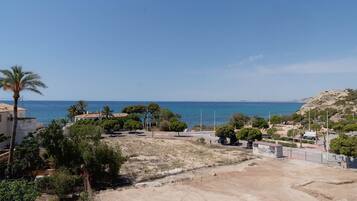 Un área residencial costera con un camino de tierra, árboles y una vista despejada del mar.