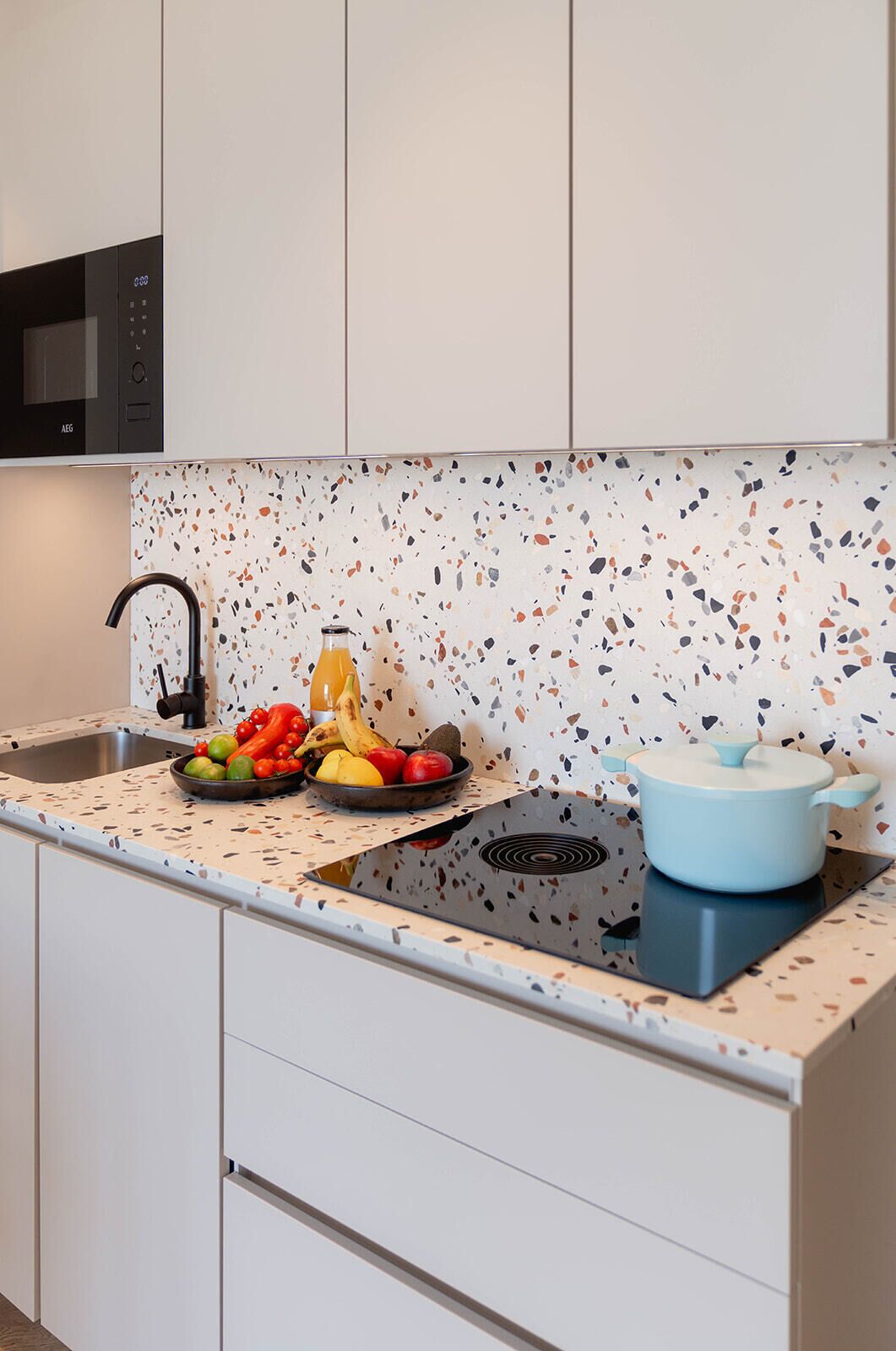 Una cocina con armarios blancos, salpicadero moteado, microondas negro, un fregadero y una olla azul sobre la estufa.