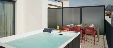 A rooftop terrace with a hot tub, outdoor seating, and a view of the city.
