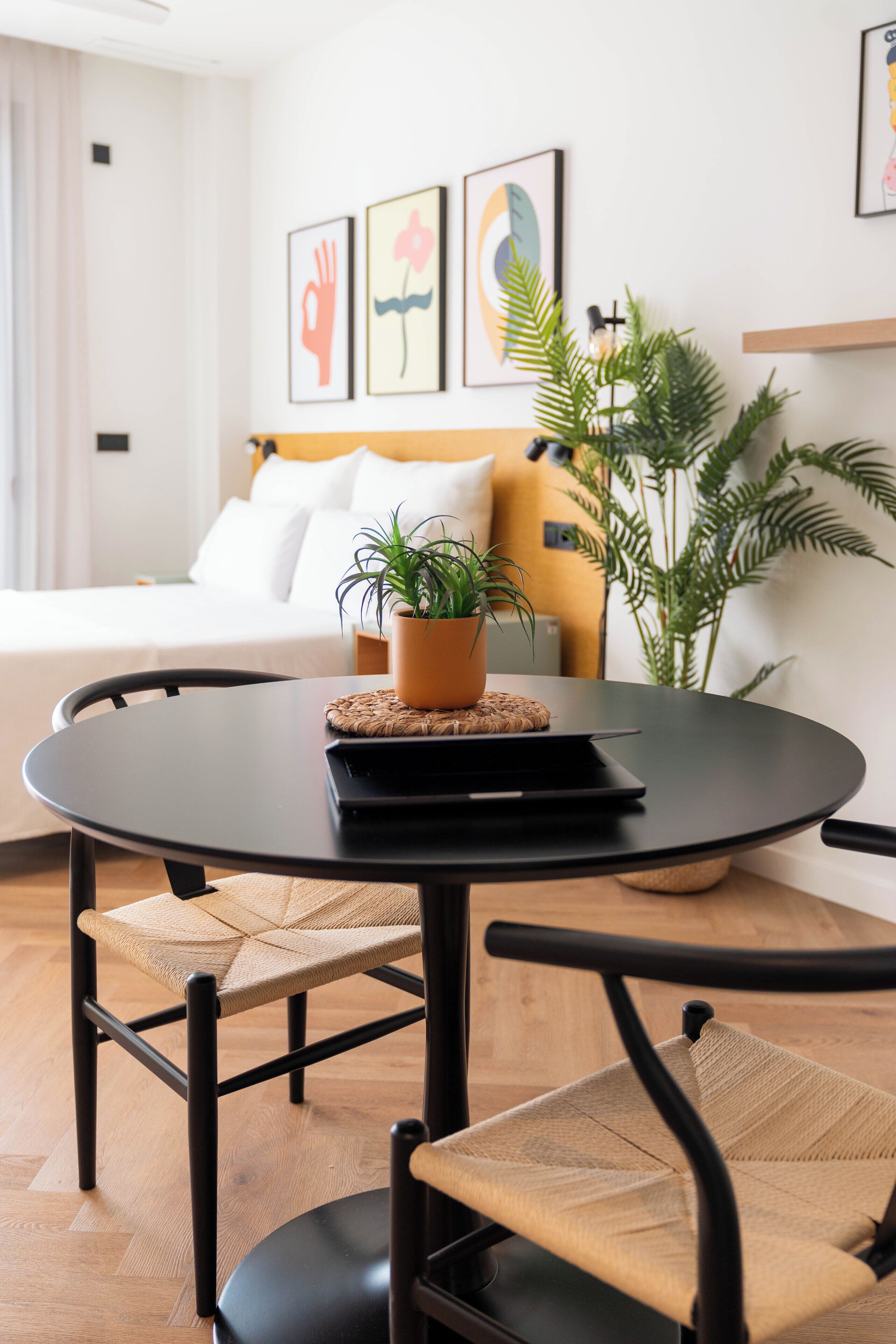 A modern hotel room with a round dining table, two chairs, a potted plant, and artwork on the wall.