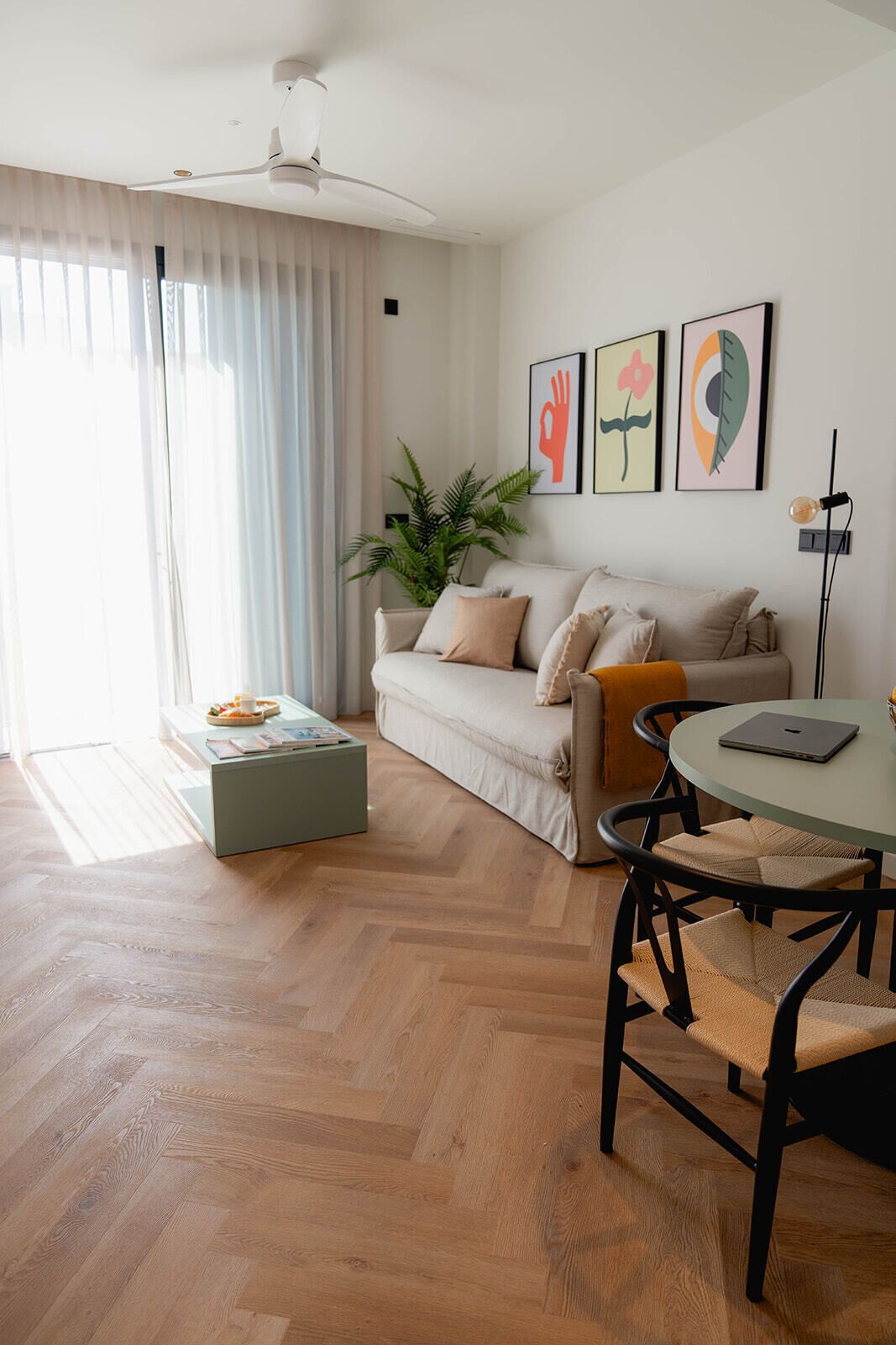 A modern living room with a sofa, a coffee table, a dining table with chairs, and artwork on the wall.