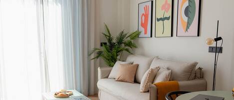 A modern living room with a sofa, a coffee table, a dining table with chairs, and artwork on the wall.