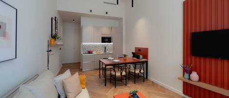 A modern apartment with a living room, dining area, and kitchen. There is a sofa, a dining table with chairs, a coffee table, and a TV mounted on the wall.