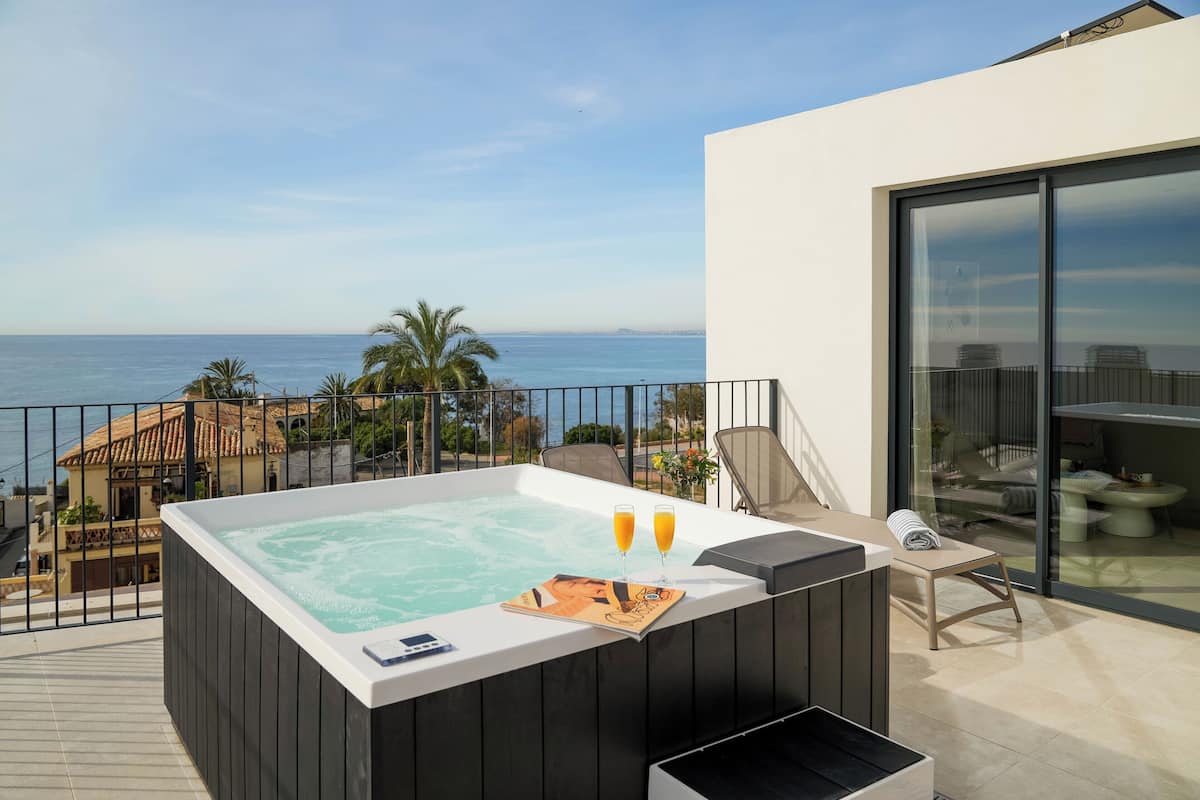 A hot tub with two glasses of orange juice on a balcony overlooking the sea.
