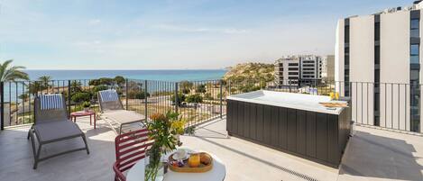A rooftop terrace with a table set for breakfast, lounge chairs, and a view of the sea.