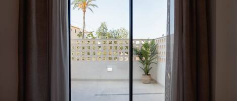 A hotel room with a large window, a bed, and a view of a courtyard with a palm tree and a potted plant.
