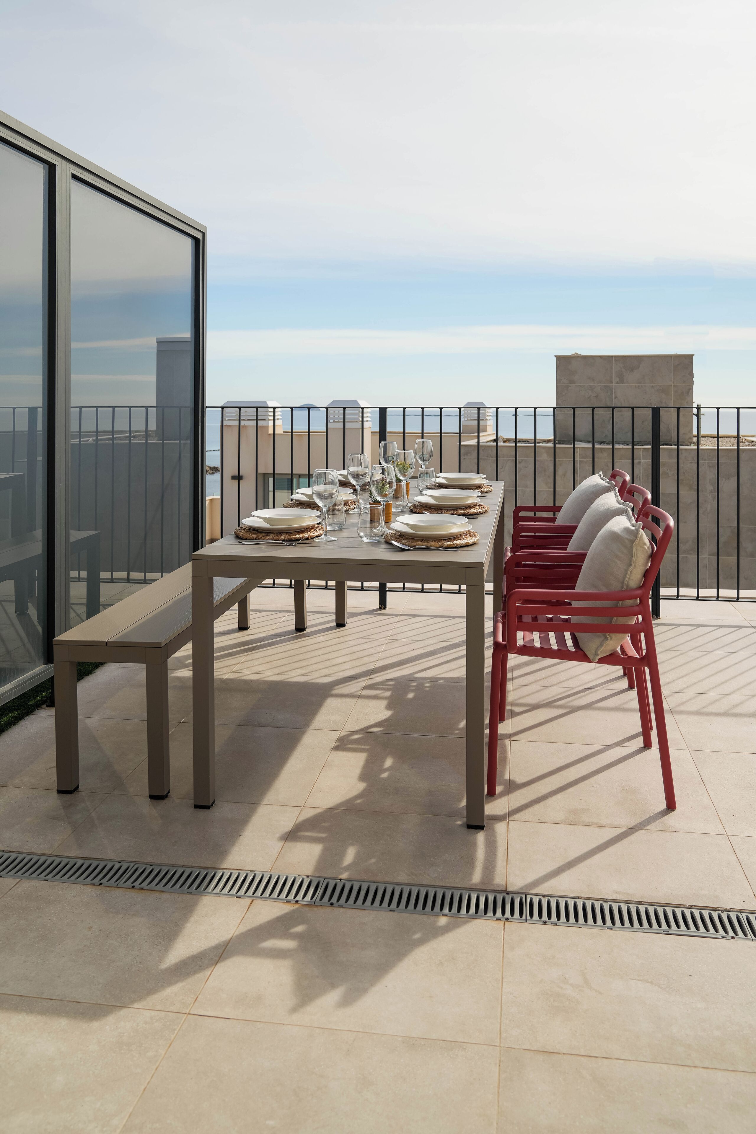 A terrace with a table set for dining, a chair, and a view of the sea.