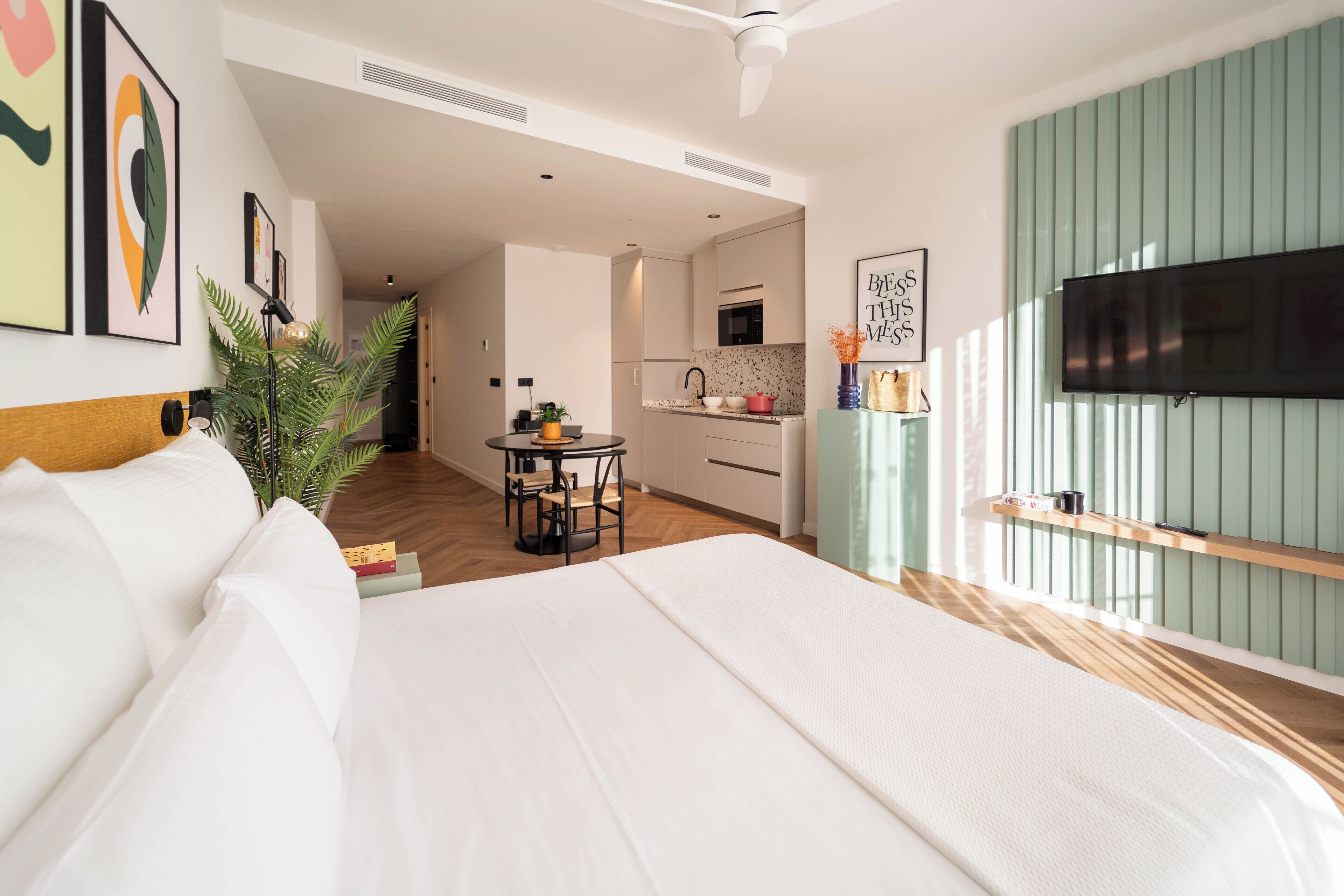 Ein modernes Hotelzimmer mit einem großen Bett, einem Esstisch, einer Küchenzeile und einem an der Wand befestigten Fernseher.