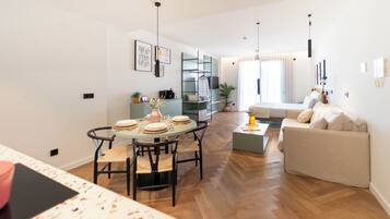 A modern living room with a sofa, a dining table with chairs, and a kitchen area in the background.