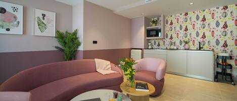 Una sala de estar moderna con un sofá curvo, una mesa de centro redonda con una computadora portátil y bebidas, y un sillón rosa.