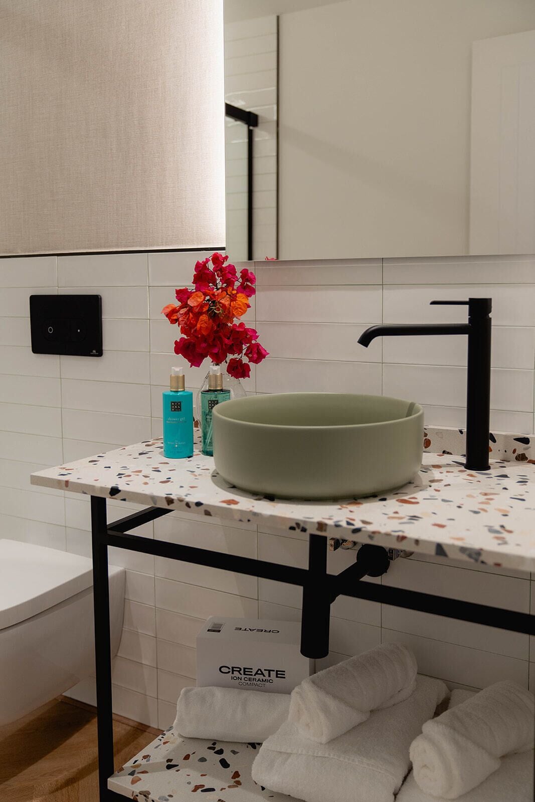 Un baño con lavamanos blanco, un espejo, toallero y encimera con un florero.