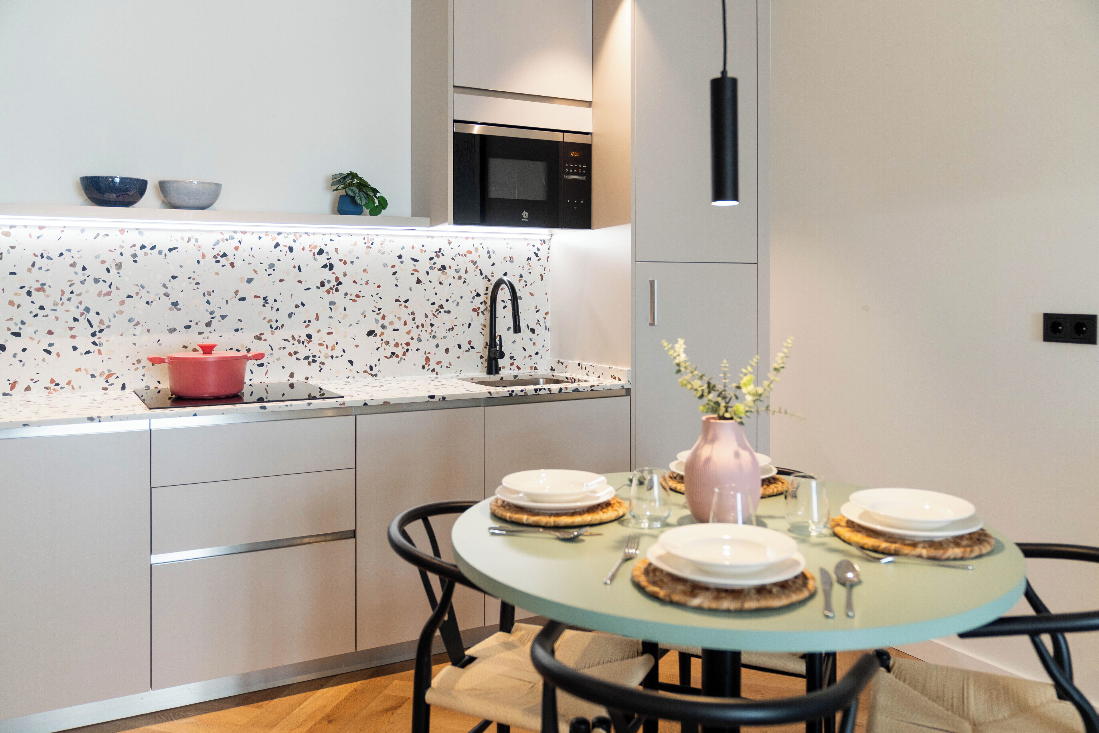 A modern kitchen with a round glass table, white cabinets, and a microwave above the counter.