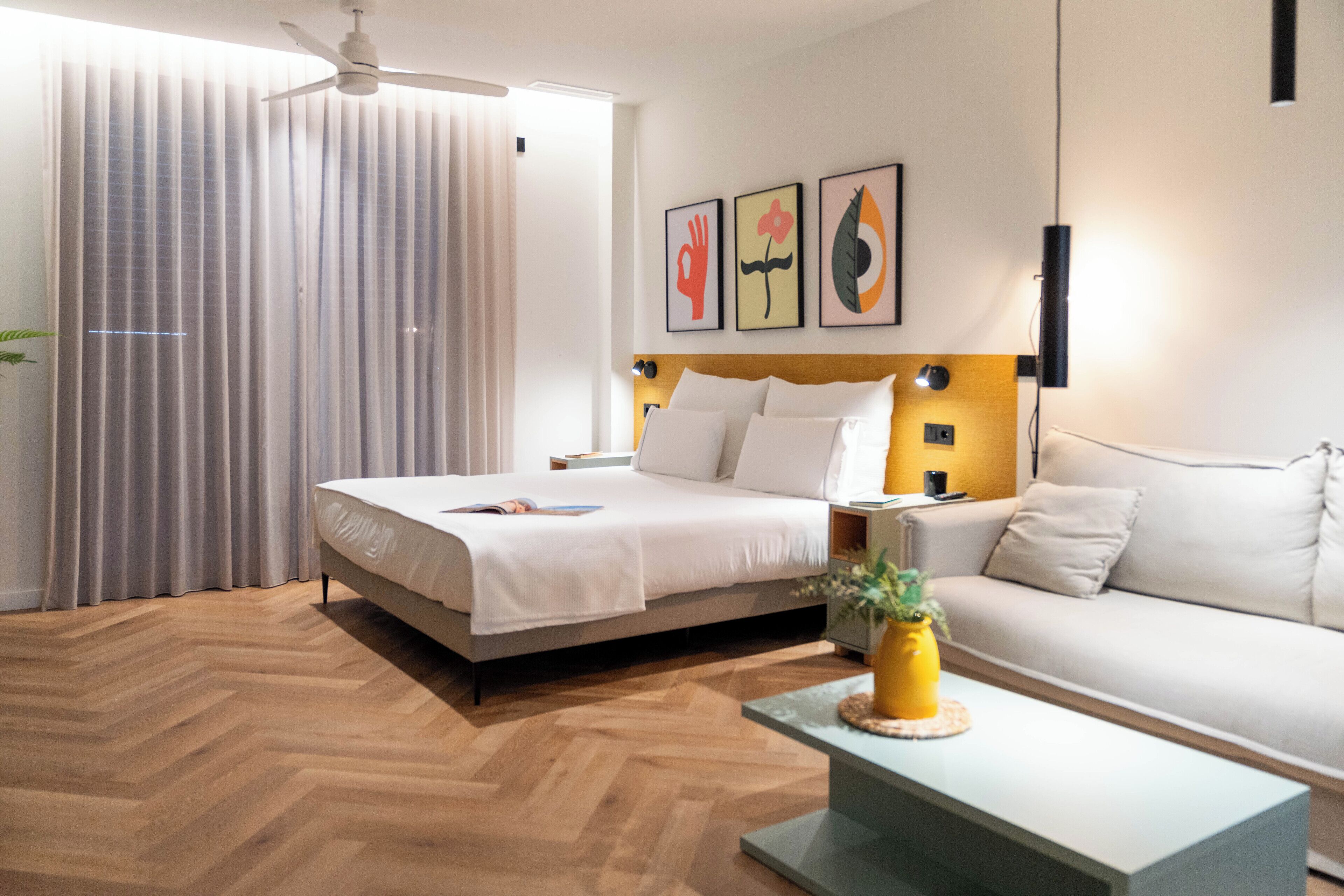 A modern hotel room with a large bed, a sofa, a coffee table, and artwork on the wall.