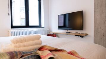 Una habitación de hotel con cama, televisor montado en la pared, ventana con persianas y radiador.