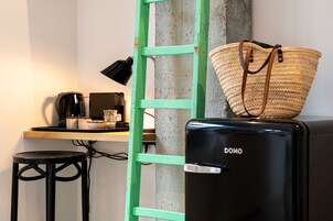 Uma cozinha compacta com cafeteira, uma mesa pequena, um banquinho e uma escada verde encostada a uma parede de concreto.