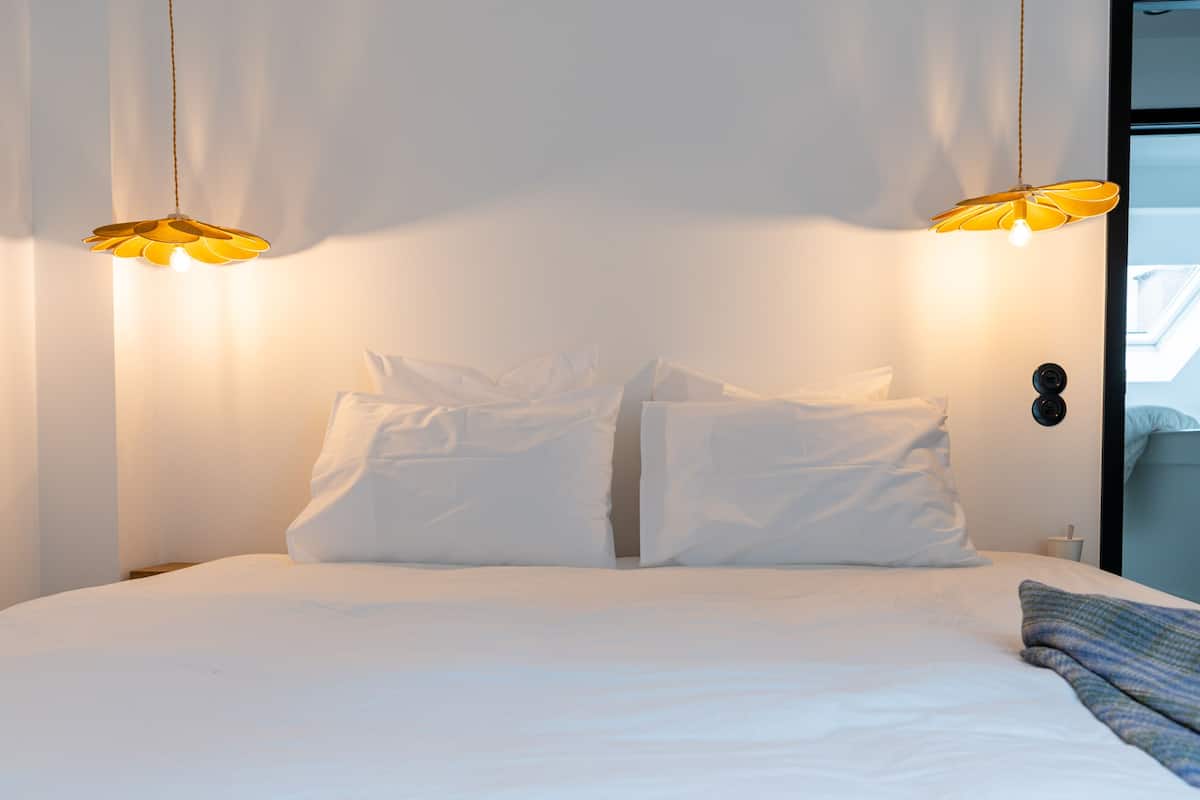 Een bed met witte lakens en twee hanglampen.