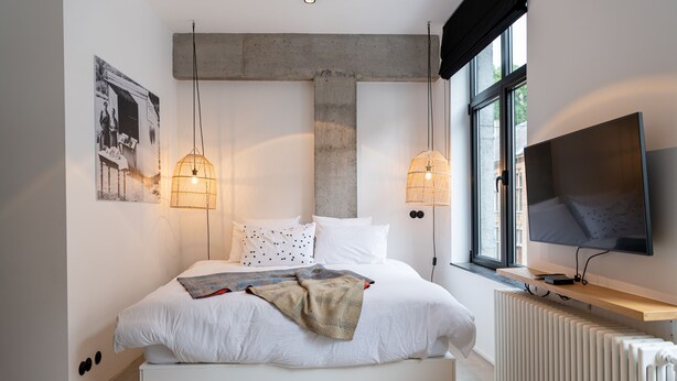 A modern bedroom with a large bed, two pendant lights, a TV, and a radiator. - Espace 43 Les 7 chambres (Namur)