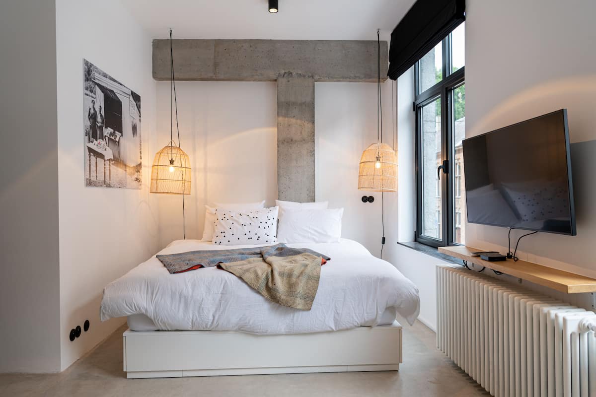 Een moderne slaapkamer met een groot bed, twee hanglampen, een televisie en een radiator.