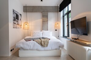 Een moderne slaapkamer met een groot bed, twee hanglampen, een televisie en een radiator.