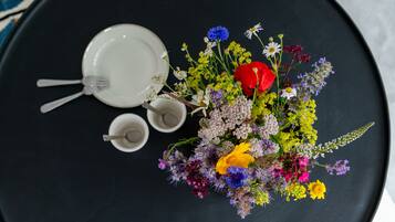 A black table with a white plate, a fork, and two small cups. A colorful bouquet of flowers is placed on the table.