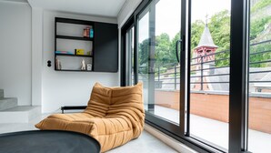 A modern room with a large window, a sofa, a black table, and a black shelving unit with books and decorative items. - Espace 43 Les 7 chambres (Namur)