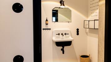 Une salle de bain avec un lavabo blanc, un miroir et une petite poubelle.