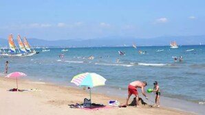 Una spiaggia con persone, una riva sabbiosa e vele a vela sull'acqua.