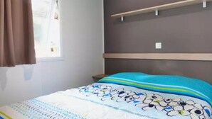 Una camera da letto con un letto, una finestra con tende, uno scaffale a parete e una parete spoglia.