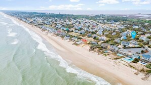 Zona residencial costera con casas a lo largo de la playa, cielo despejado y vista al océano.
