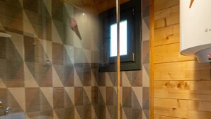 Un área de ducha con puerta de vidrio, paredes de madera y una ventana pequeña.