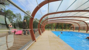 An indoor swimming pool with a transparent roof and wooden deck.