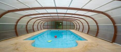 An indoor swimming pool with a curved ceiling and tiled floor.