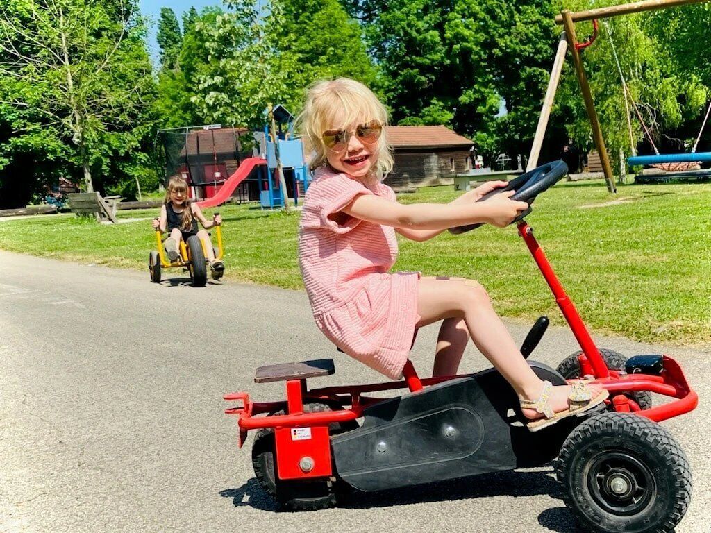 Un enfant circule sur une trottinette électrique rouge sur un chemin aménagé dans un parc.