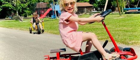 A child riding a red electric scooter on a paved path in a park.