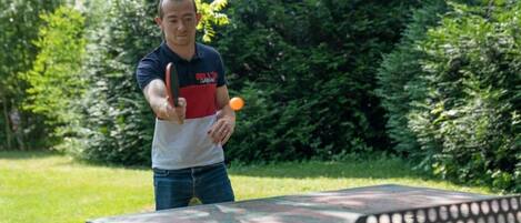 A person playing ping pong outdoors with a table and a ball.