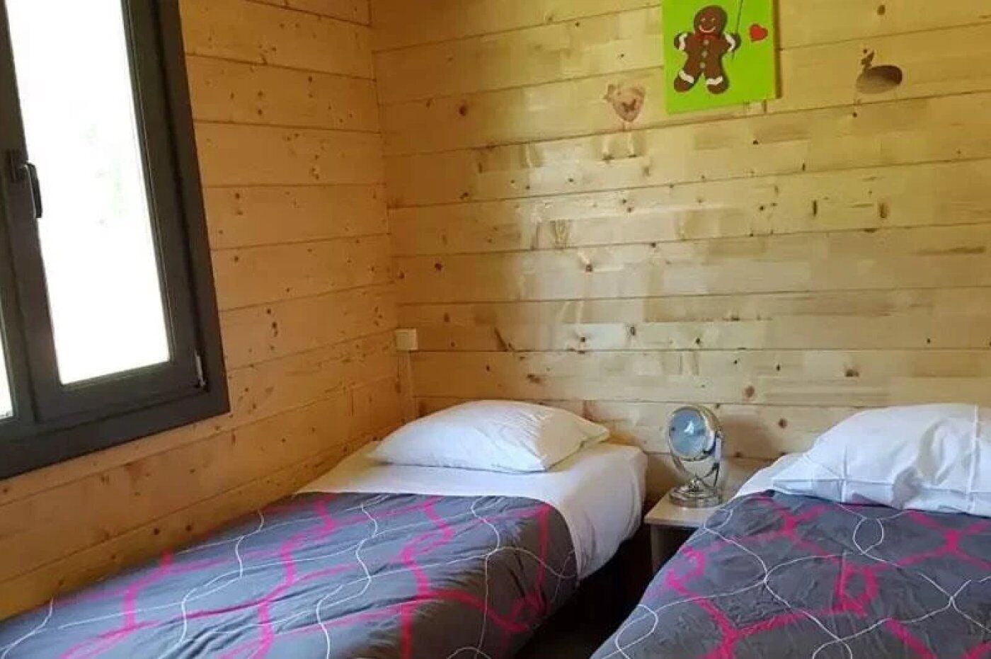 A small room with two beds, wooden walls, a window, and a wall decoration.