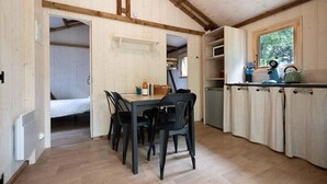 A compact kitchen with wooden cabinets, a dining table with chairs, and a window providing natural light. - ZEcamping 2 étoiles piscine couverte dog friendly jacuzzi locatif BBQ 27m2 (Bar-sur-Aube)