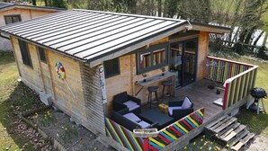 Une cabane en bois avec un toit en métal, une terrasse dotée de coussins rayés aux couleurs vives et un petit espace extérieur aménagé pour s’asseoir.