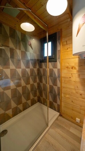 Ein Duschbereich mit Glastür, Holzwänden und einem kleinen Fenster.