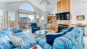 A spacious living room with a large sofa set, a ceiling fan, a fireplace, and a television. - The beautiful beaches of Corolla are just a few feet away at Oasis! (Corolla)