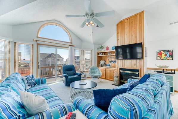 A spacious living room with a large sofa set, a ceiling fan, a fireplace, and a television.