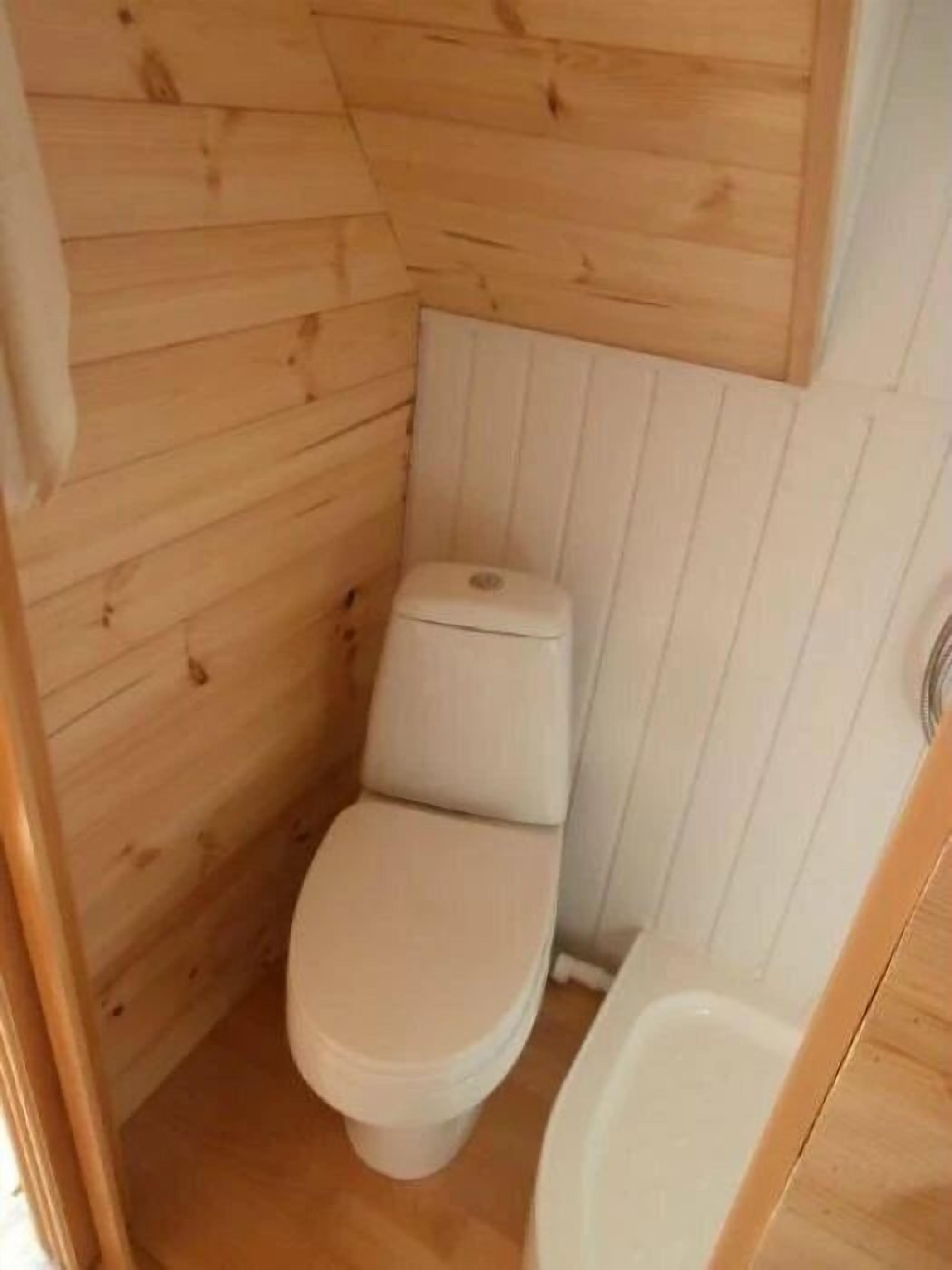 A small, wooden-paneled bathroom with a toilet and a bathtub.