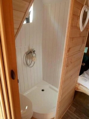 Un baño pequeño y cerrado con inodoro, zona de ducha y paneles de madera.