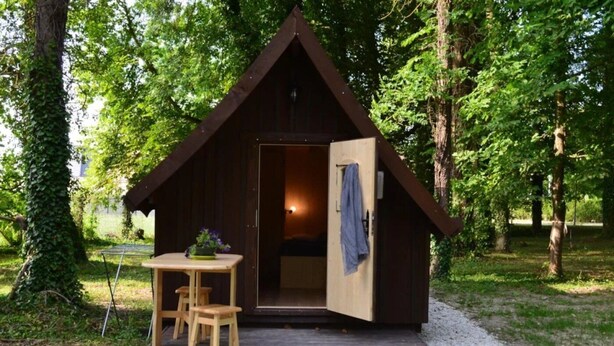 A small wooden cabin with an open door, a table with chairs, and a potted plant outside.