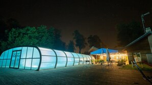 A greenhouse structure with a transparent roof, a wooden deck, and a small outdoor seating area with tables and chairs.