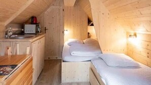 A compact wooden cabin with a loft bedroom, a small kitchenette, and a wooden dining table.